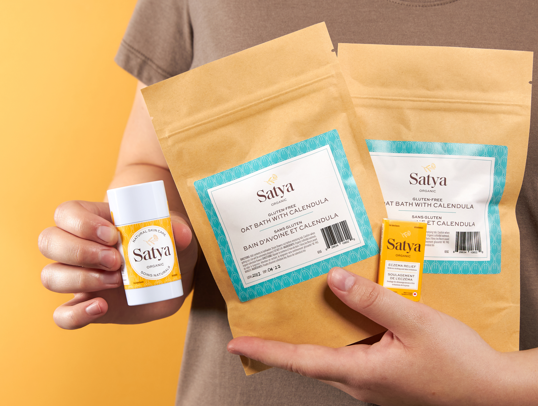 Person holding two Calendula Oat Baths, a Satya Eczema Relief Easy Glide Stick. and a Satya Eczema Relief travel tin.