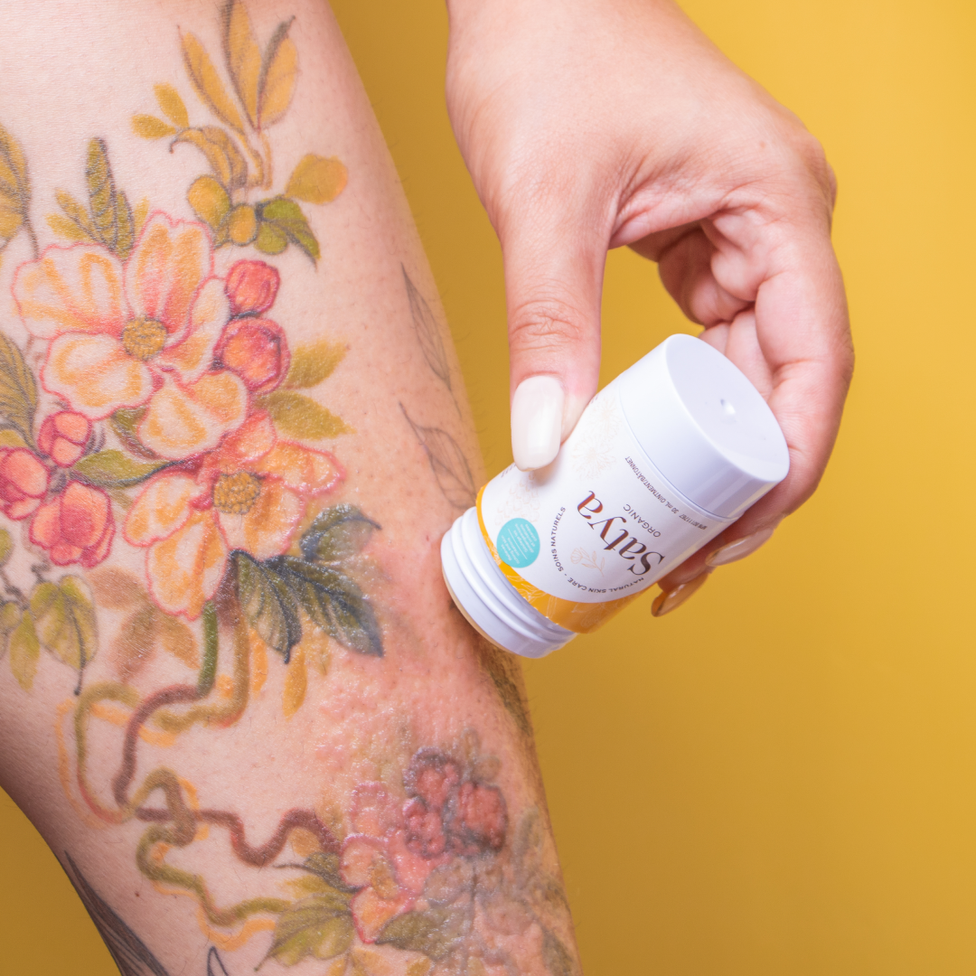 A person applying Satya Eczema Relief Easy Glide Stick to irritated skin on their tattoo.