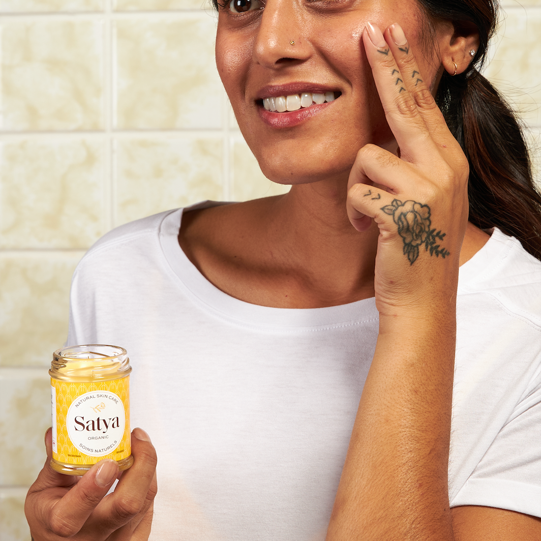 A person applying Satya Eczema Relief from the jar to their face. 